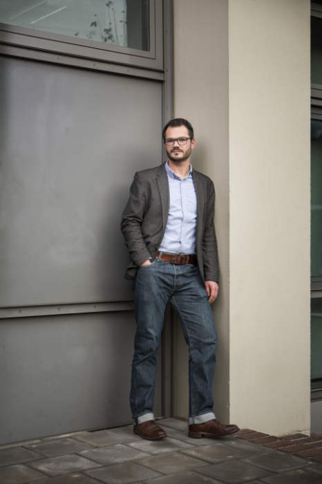 Prof. Robert Böhm lehnt gelassen an einer Wand und blickt in die Kamera